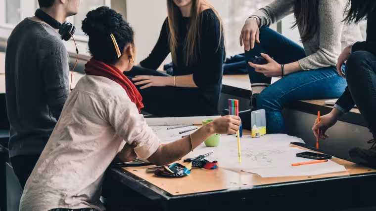 Mehrere Studierende sitzen um einen Tisch und diskutieren über ein Projekt