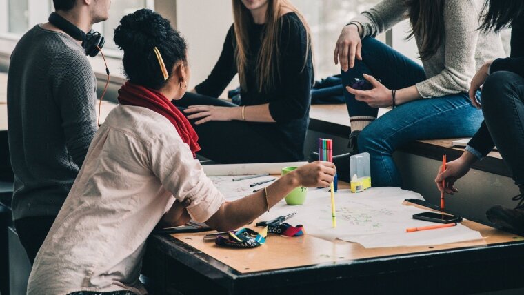 Mehrere Studierende sitzen um einen Tisch und diskutieren über ein Projekt