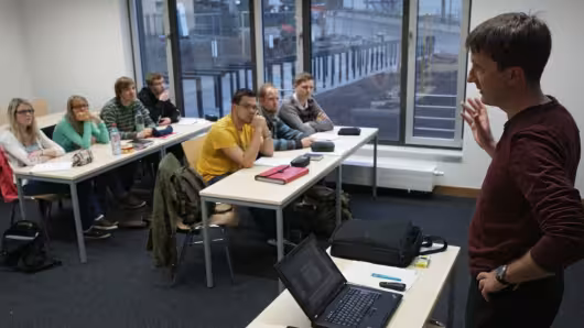Lehrender spricht zu Studierenden im Seminarraum