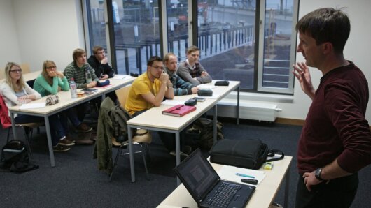 Lehrender spricht zu Studierenden im Seminarraum