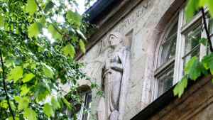 Blick auf die Figur der Fakultät für Rechtswissenschaften am 25.07.2023 an der Friedrich-Schiller-Universität Jena in Jena. Die Nordfassade des Universitätshauptgebäudes wird von mehreren baukünstlerischen Elementen verziert. So sind die damaligen Fakultäten im Form von allegorischen Frauenstatuen auf der Höhe des dritten Stockwerkes zu sehen. 1908 waren vier Fakultäten an der Universität ansässig: die Theologie, die Rechtswissenschaften, die Medizin und die Philosophie. Die Figuren sind in Roben gehüllt. Die Attribute, sowie die über ihnen in den Stein gehauenen Benennungen, machen sie eindeutig zu ortbar. Die Rechtswissenschaft hält in den Händen das richtende Schwert, zu ihren Füßen das Gesetz in Form eines Buches.