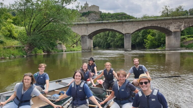 Teammitglieder in Kanadiern auf der Saale vor einer Brücke und der Rudelsburg