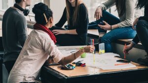 Several students sit around a table and discuss a project